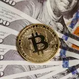 A vertical shot of a Bitcoin coin placed on multiple hundred-dollar bills symbolizing cryptocurrency and traditional finance.