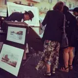 Art enthusiasts browsing paintings at an outdoor market in Roma, Italy.