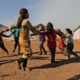 Children joyfully play outdoors in a Syrian refugee camp, forming a lively circle.