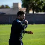 Football coach blowing a whistle during practice on a sunny day outdoors.