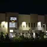 Edificio de almacén de Amazon iluminado por la noche con árboles y señalización.