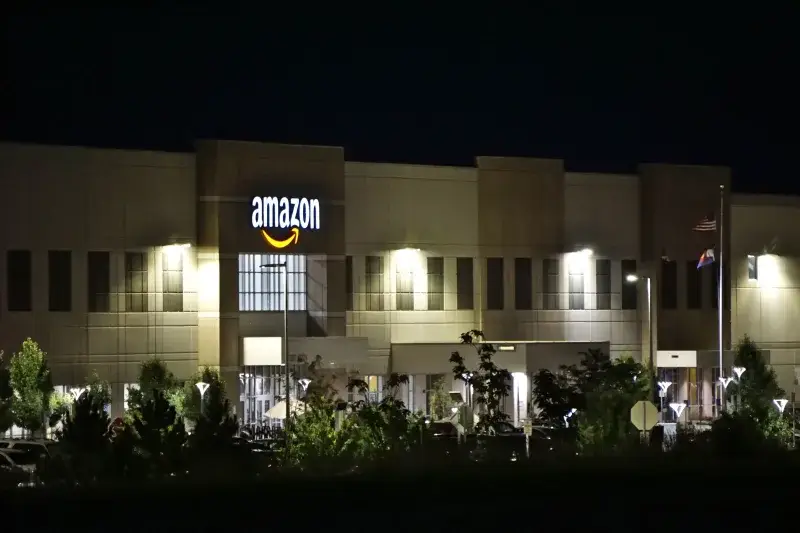 Edificio de almacén de Amazon iluminado por la noche con árboles y señalización.