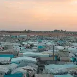 Aerial photo of a sprawling refugee camp under a vibrant sunset sky