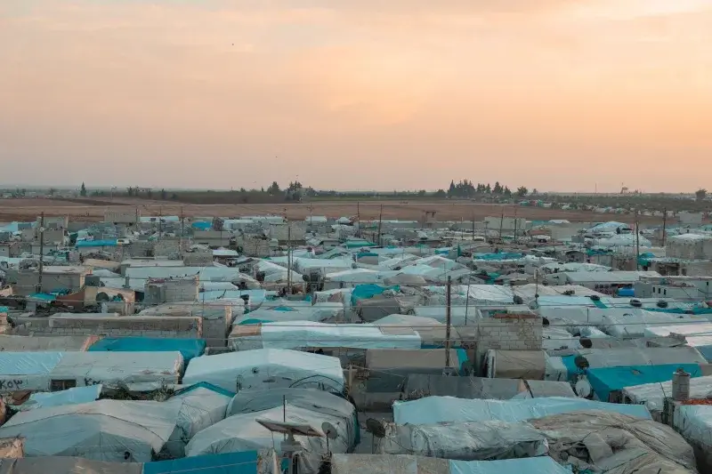 Aerial photo of a sprawling refugee camp under a vibrant sunset sky