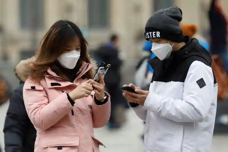 Una pareja con mascarillas revisa sus teléfonos móviles cerca de la Pirámide del Louvre, en París, Francia.