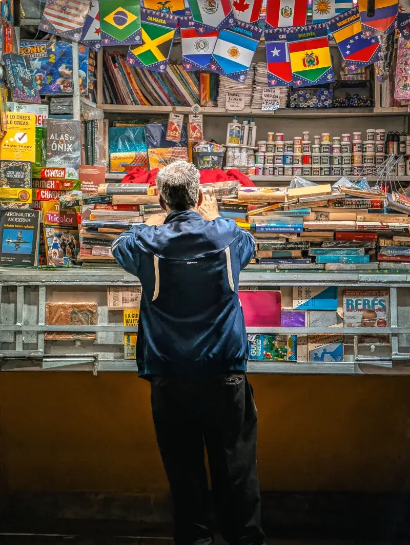 Un hombre examina libros en un quiosco colorido decorado con banderas internacionales en Venezuela.