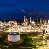 Aerial night view of a brightly lit industrial oil refinery with smoking chimneys in Rosemount, MN, USA.