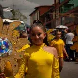 A vibrant street parade in Mérida, Venezuela, with participants in yellow costumes holding sun decorations.