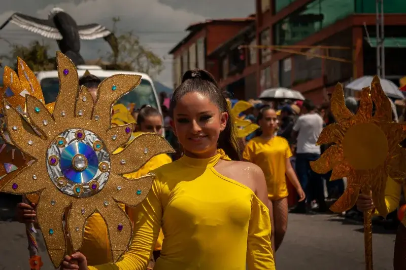 A vibrant street parade in Mérida, Venezuela, with participants in yellow costumes holding sun decorations.