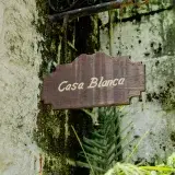 A wooden Casa Blanca sign hangs on a weathered stone wall surrounded by lush greenery.