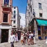 Lively street view in Venice with tourists exploring shops and architecture under a bright summer sky.