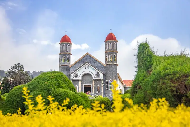 Exterior of historic Iglesia de San Rafael Catholic church in Costa Rica located in beautiful garden with green and yellow plants