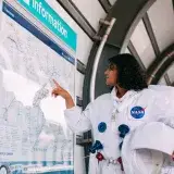 Person in a NASA spacesuit pointing at a London Underground map. Futuristic travel concept.