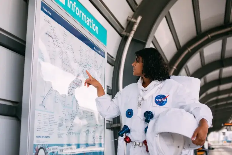 Person in a NASA spacesuit pointing at a London Underground map. Futuristic travel concept.