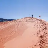 Three hikers atop the vibrant Coral Pink Sand Dunes in Utah under a clear blue sky.