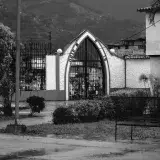Monochrome image of a gothic-style cemetery gate in Mérida, Venezuela, with Andes mountains in the backdrop.