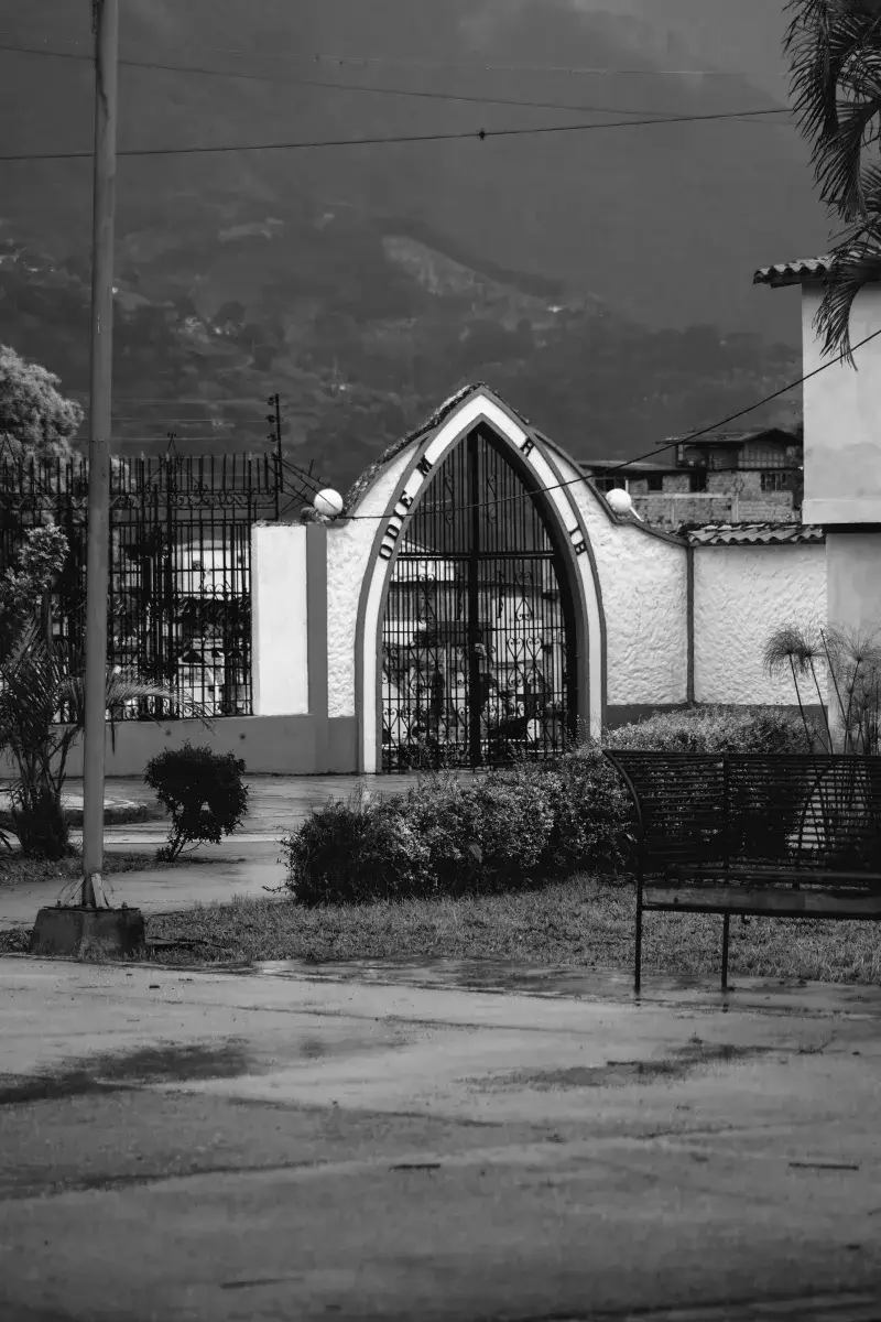 Monochrome image of a gothic-style cemetery gate in Mérida, Venezuela, with Andes mountains in the backdrop.