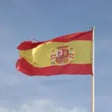 Spanish flag waving on a tall flagpole against a clear blue sky in El Puerto de Santa María, España.
