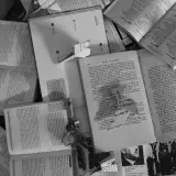 A black and white artistic arrangement of various open books and paper crafts, creating a conceptual still life.