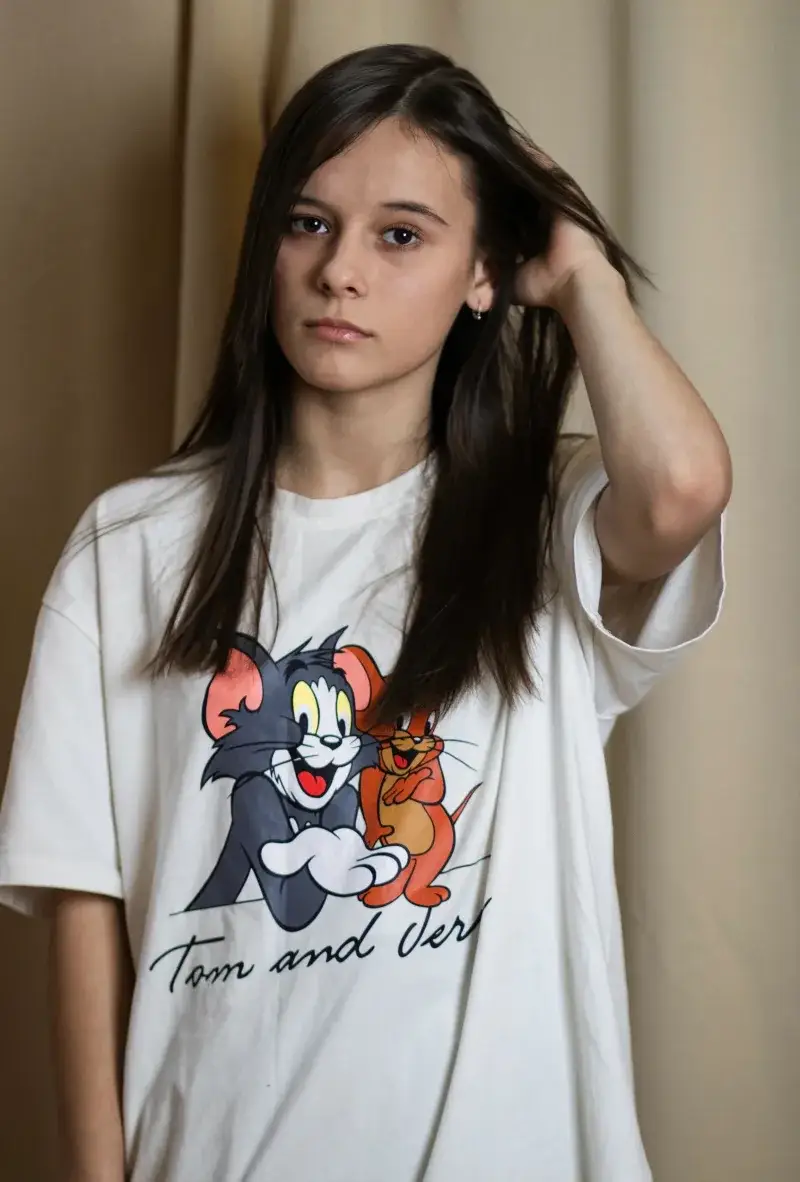 Portrait of a young woman fixing her hair, wearing a 'Tom and Jerry' t-shirt, on a studio backdrop.