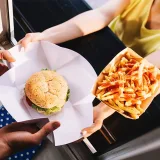 A food server hands a hamburger and some fries to a customer