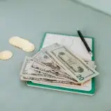 Close-up of American dollar bills and coins on a journal with a pen, representing budget planning.