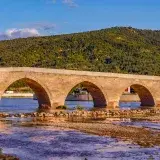 Stunning view of a historic stone arch bridge in Çorum, Türkiye surrounded by lush hills and calm river.