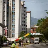 A lively urban scene in Venezuela featuring a colorful footbridge, high-rise residential buildings, and bustling street life.