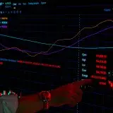A hand points to cryptocurrency graphs on a trading screen indicating market analysis.