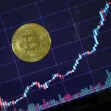 Gold Bitcoin on screen with rising investment chart indicating cryptocurrency growth.