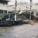 A damaged vehicle and debris on an urban street after a fire incident, depicting aftermath and destruction.