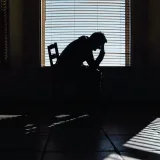 A man holds his head in his hands as he sits on a bed