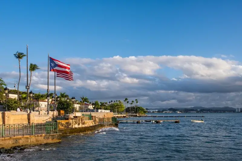 Unavista pintoresca del frente marítimo de Puerto Rico con una bandera ondeando contra el fondo del mar y el paisaje urbano.