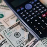 From above of electronic calculator placed over American cash paper money for budget planning and income and expenses calculation