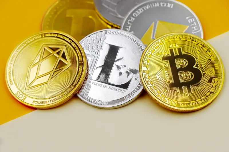 Close-up of various cryptocurrency coins including Bitcoin, EOS, and Litecoin on a colorful background.