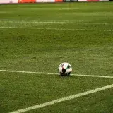 A soccer ball rests on a well-maintained green football field corner, ready for play.