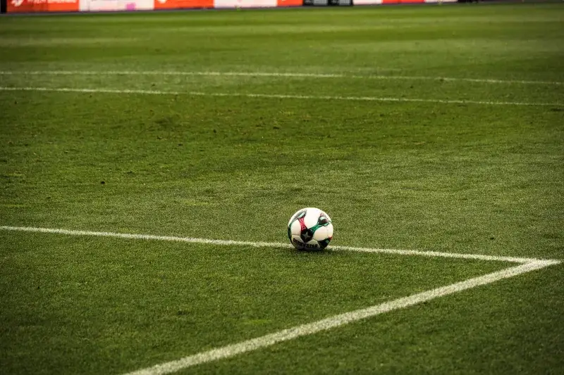 A soccer ball rests on a well-maintained green football field corner, ready for play.