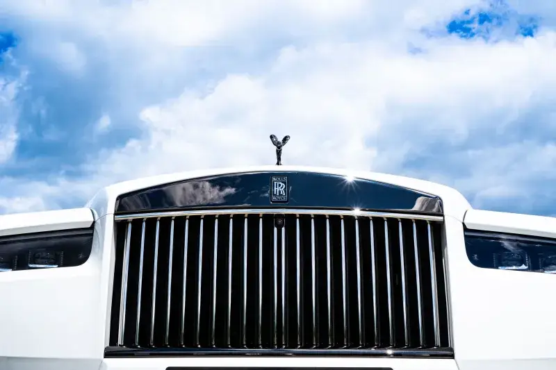 Close-up of a white Rolls-Royce with a distinctive grille under a bright blue sky, showcasing luxury design.