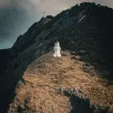 Scenic view of Cape Brett Lighthouse perched on a rugged hillside in Northland, New Zealand under dramatic skies.
