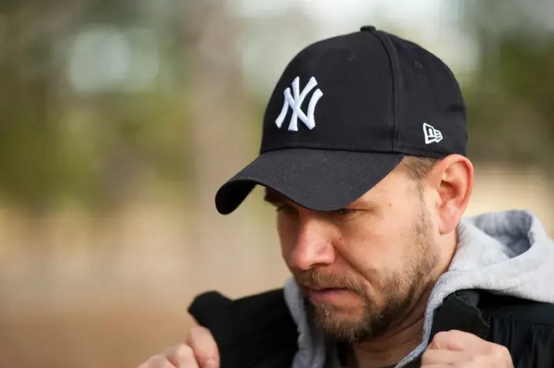 Close-up portrait of a man in a black New York Yankees cap outdoors, focusing on his face.