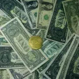 A golden bitcoin coin surrounded by scattered US dollar bills, symbolizing the contrast between digital and traditional currency.