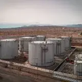 Aerial view of large industrial oil tanks in a desert setting with mountains in the distance.