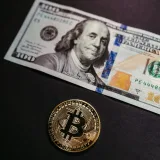 Close-up of a Bitcoin coin with a US 100 dollar bill, symbolizing digital and traditional currency.