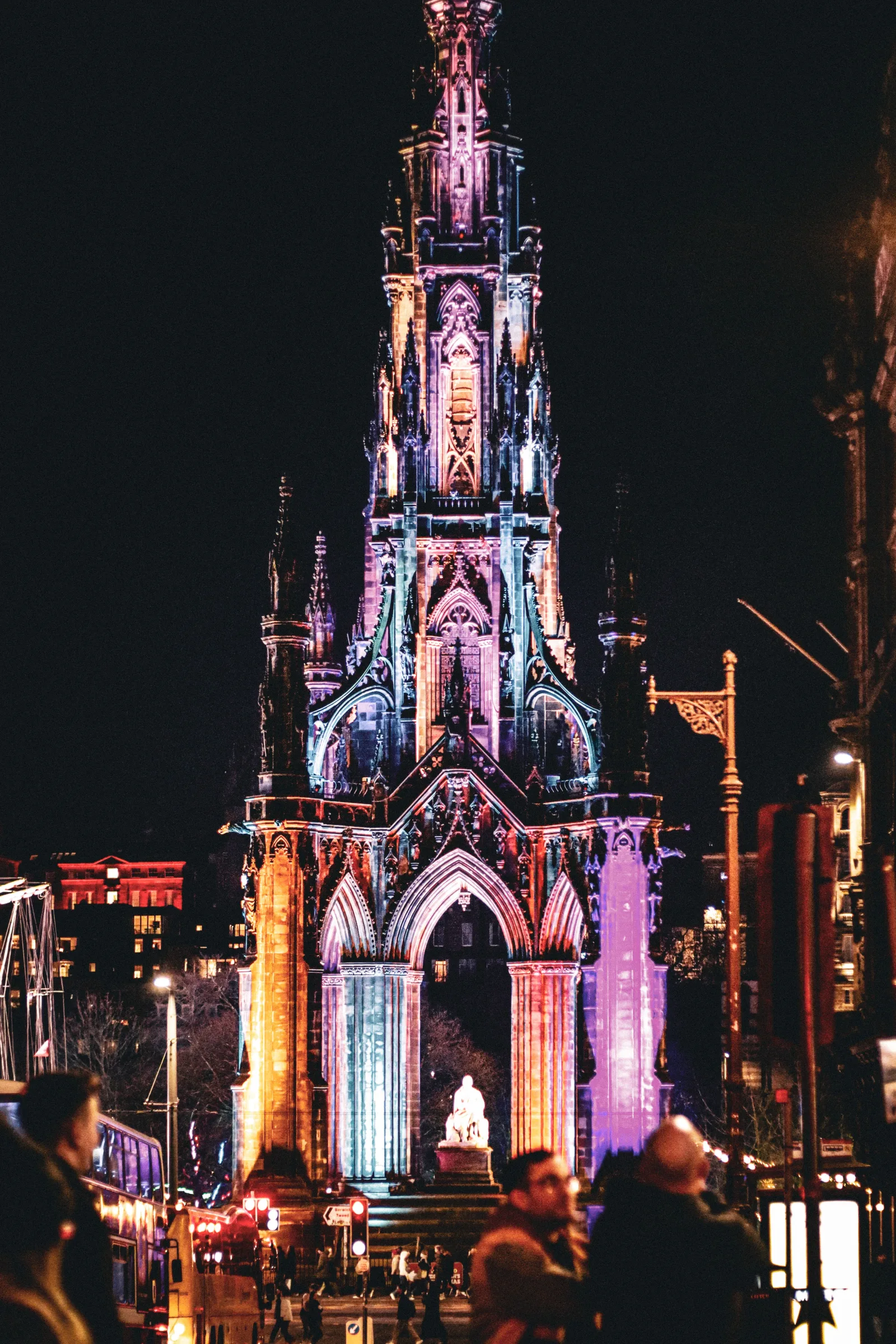 Vibrantly lit Scott Monument in Edinburgh, Scotland at night with a lively urban atmosphere.