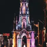 Vibrantly lit Scott Monument in Edinburgh, Scotland at night with a lively urban atmosphere.