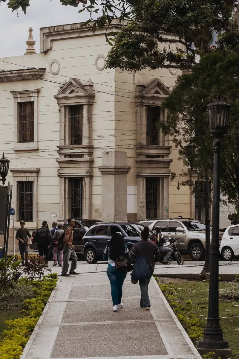 People walking on a street in Mérida, Venezuela, featuring historic architecture and parked cars.