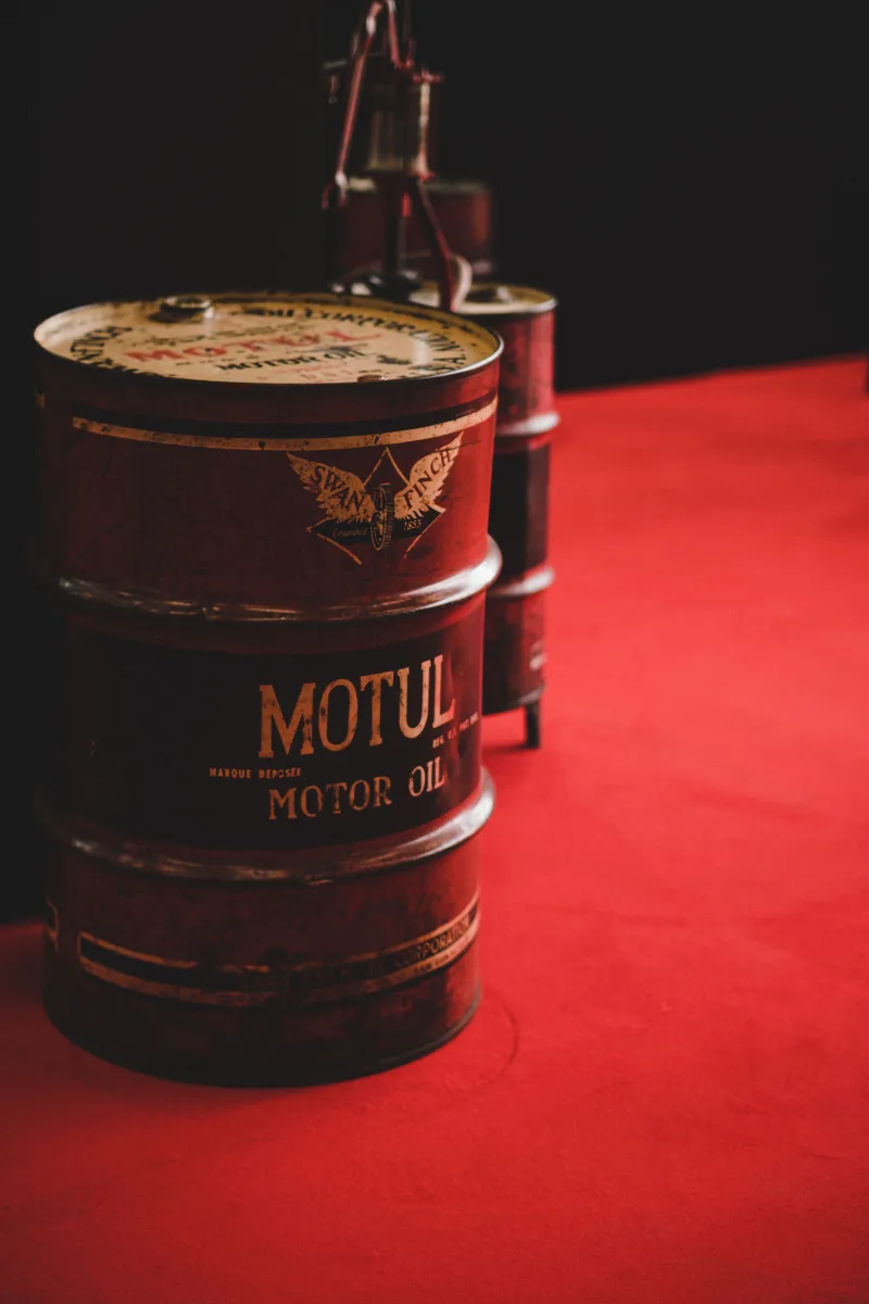 A close-up of a rusty oil barrel in an industrial setting with a red backdrop.