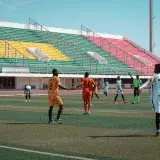 Energetic football match with players in orange and white, vibrant stadium backdrop.