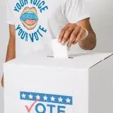 Primer plano de una persona colocando un voto en una urna, resaltando la participación electoral.