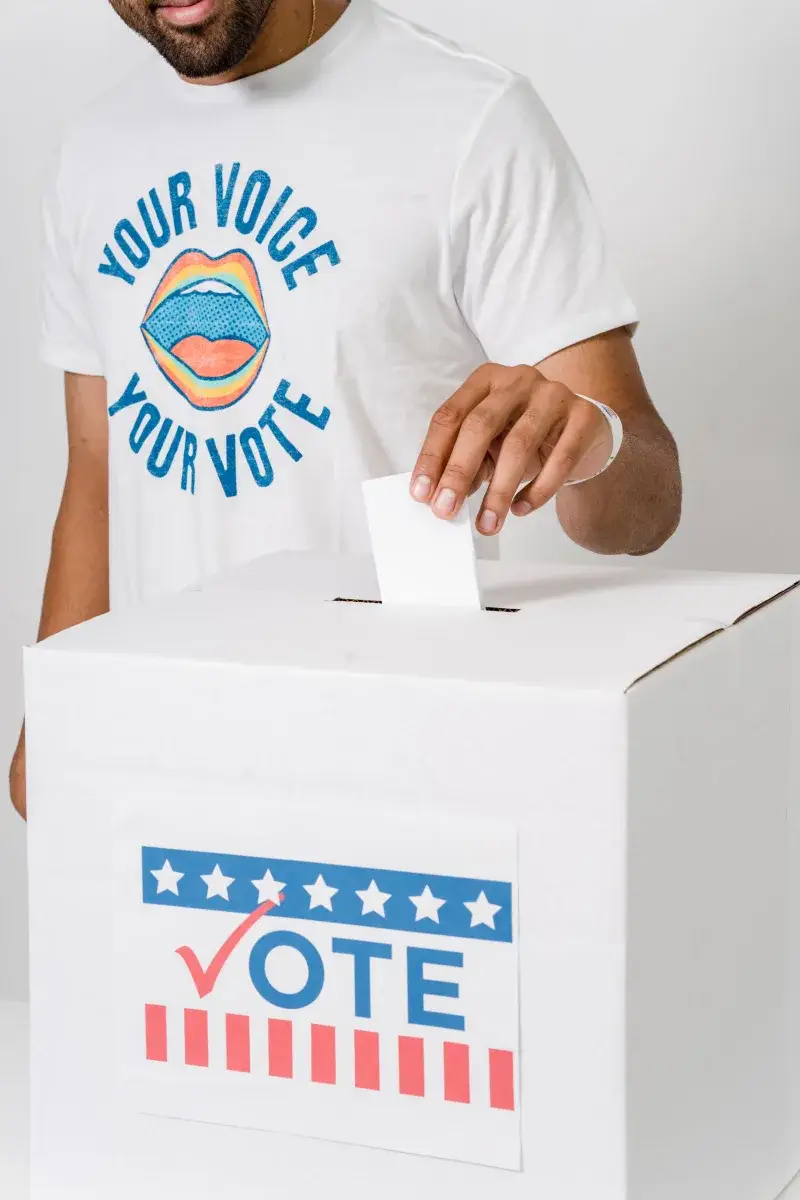 Primer plano de una persona colocando un voto en una urna, resaltando la participación electoral.